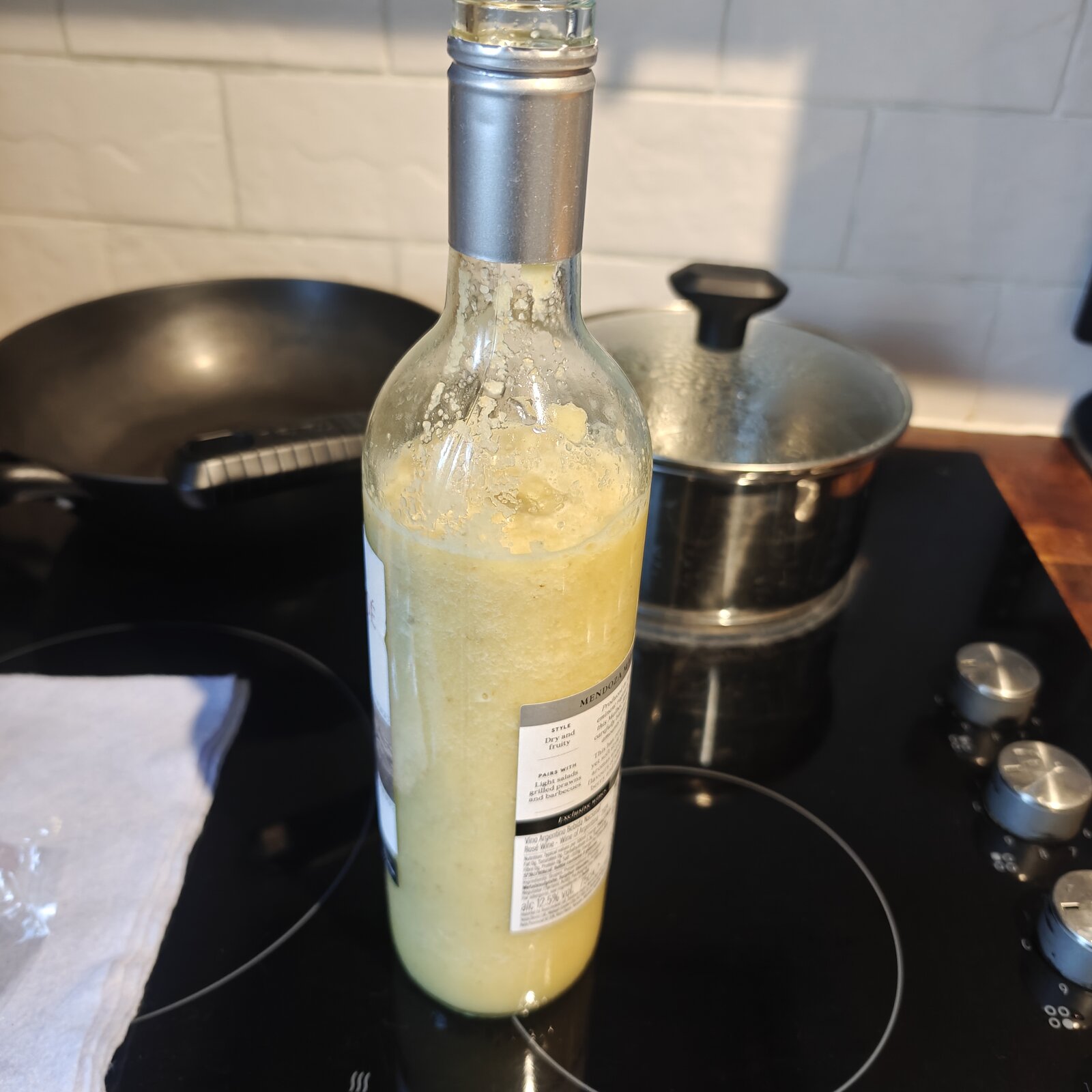 Recycled Malbec Rose wine bottle of v1 ginger shot, sitting on the hob. Thick pulp clinging to the inside walls. Consistency was too thick to drink straight.